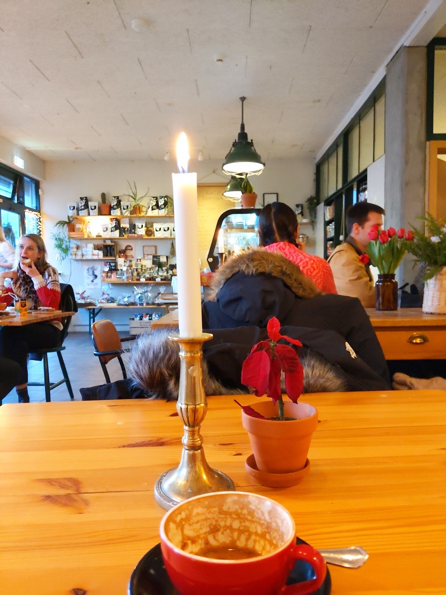 Inside a café in Reykjavik, a red coffee cup on a pine table with a lit candle and small Poinsettia flower next to it.